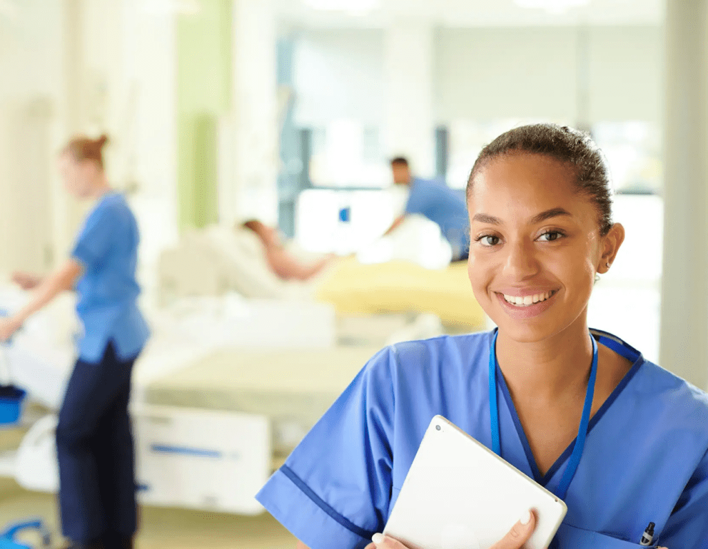 Smiling nurse holding a tablet in a hospital room.
