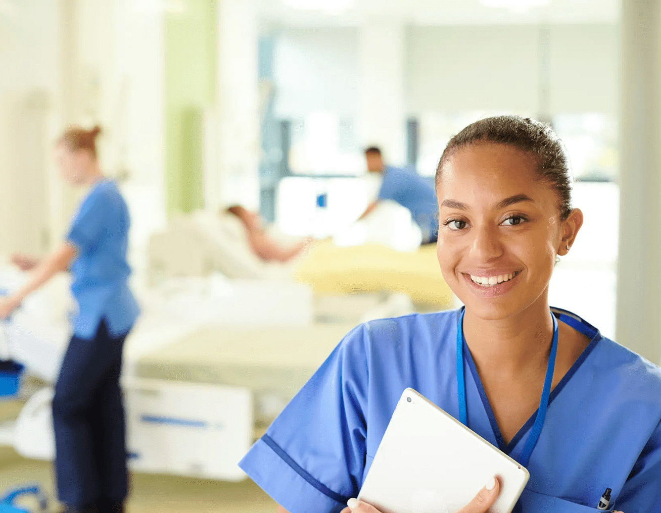 Smiling nurse holding a tablet in a hospital room.