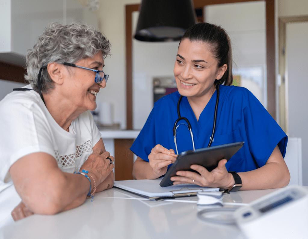 A nurse consulting with an elderly woman, both smiling.