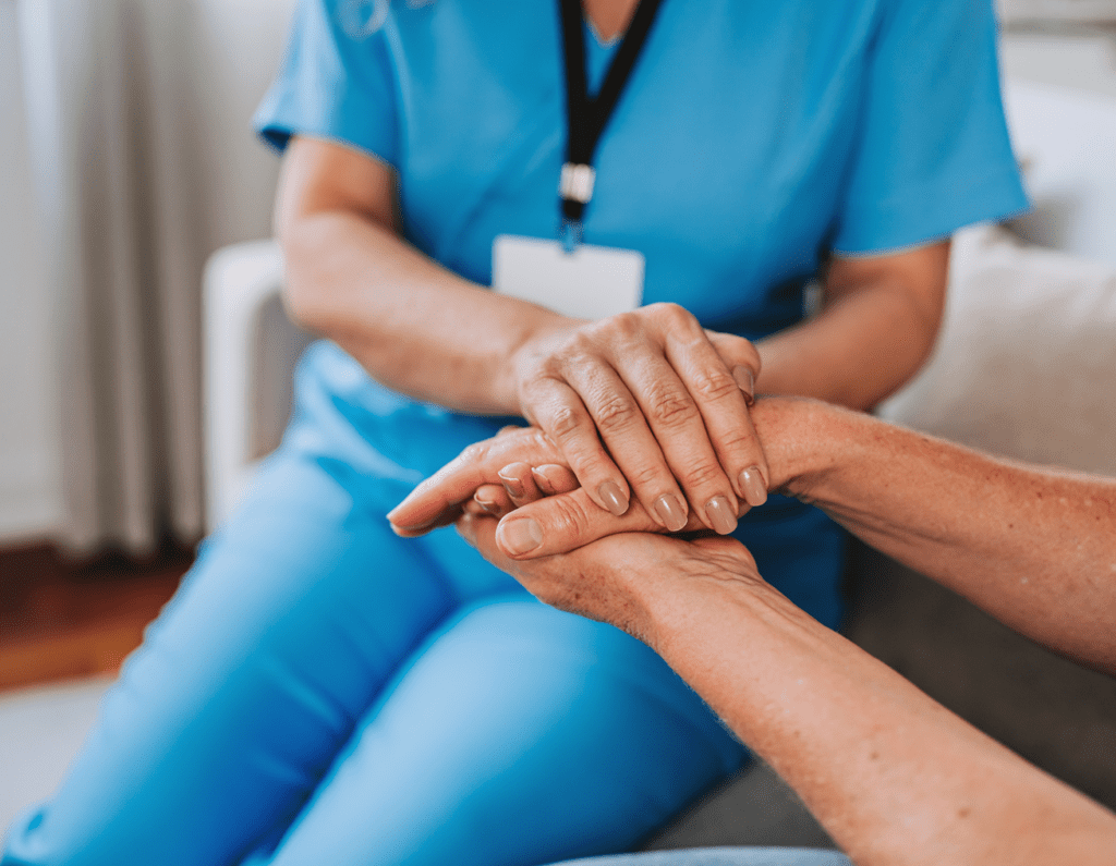 A healthcare worker holding a patient's hand in a comforting gesture.